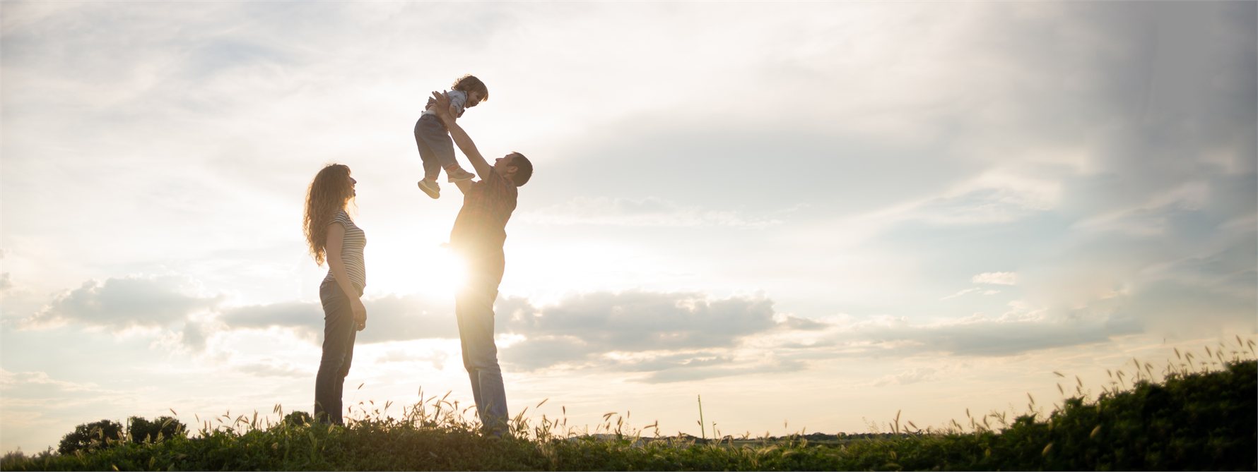 Genitori che sollevano il loro bambino in un prato al tramonto