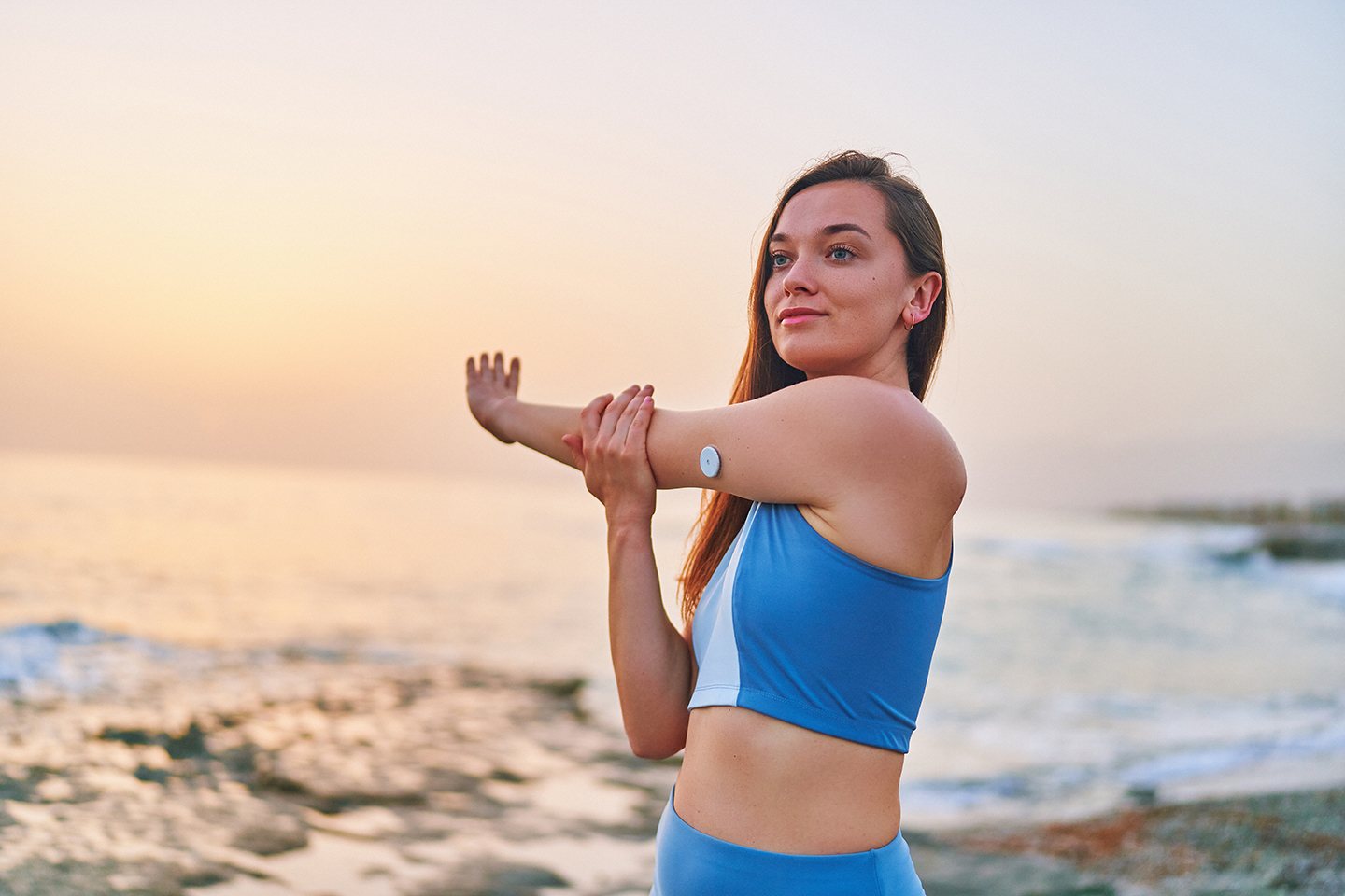 Donna che fa stretching del braccio in riva al mare al tramonto